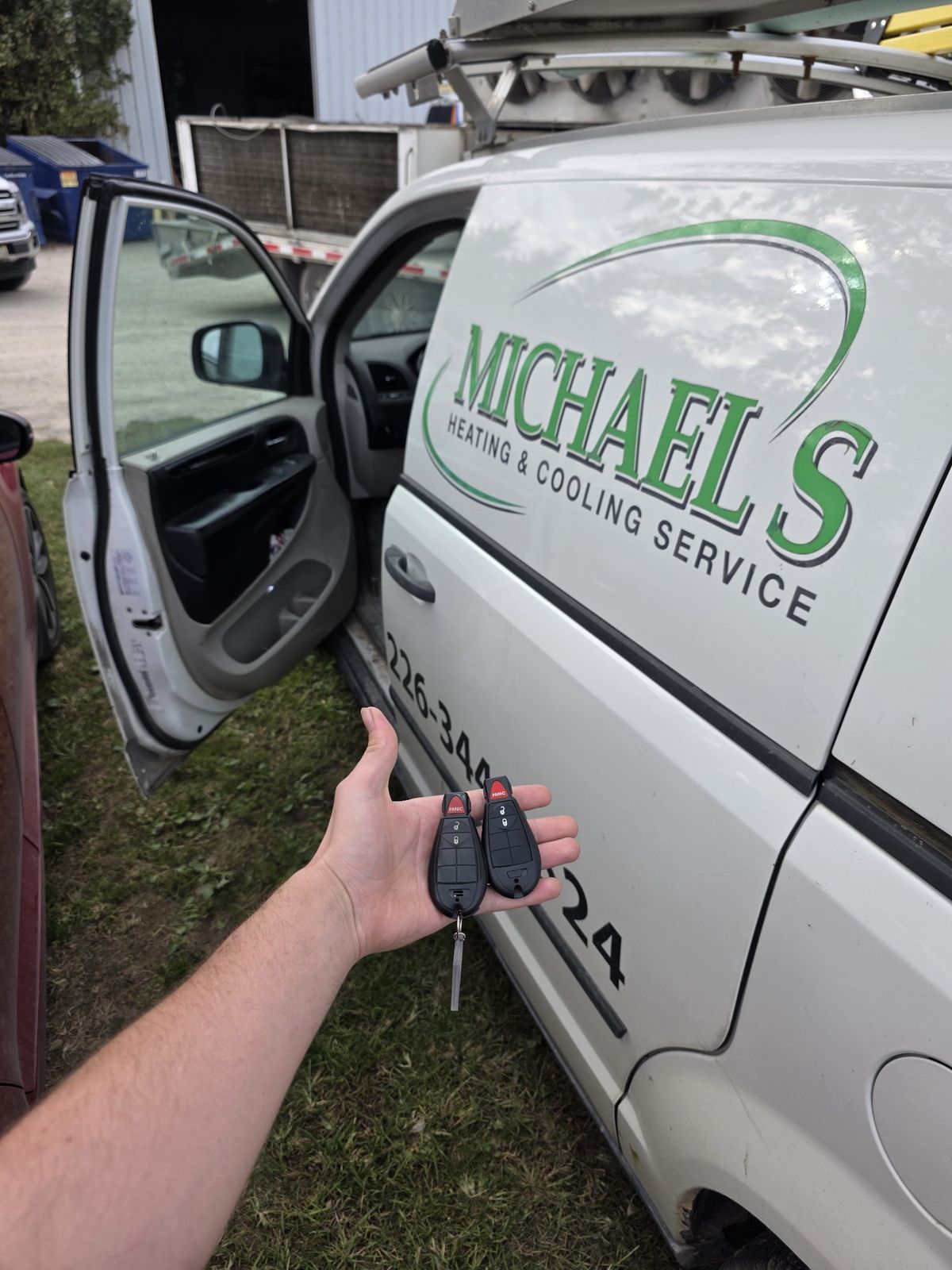 Two newly made Dodge FOBIK keys held beside a lettered heating and cooling service van