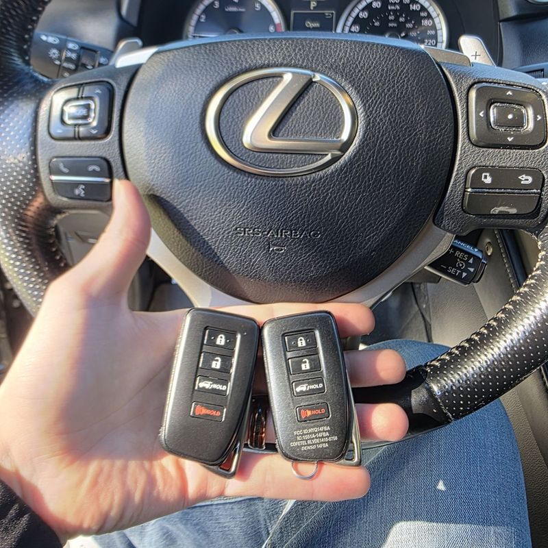 Two Lexus smart key fobs held at a Lexus steering wheel