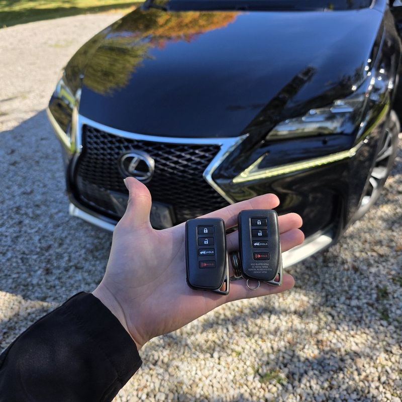 Two Lexus smart keys held in a hand in front of a black Lexus NX